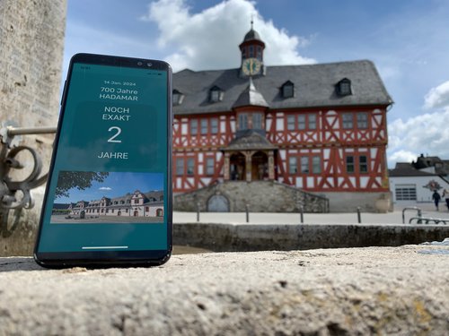 Ein Smartphone mit einem Countdown zum Jubiläum vor dem Rathaus