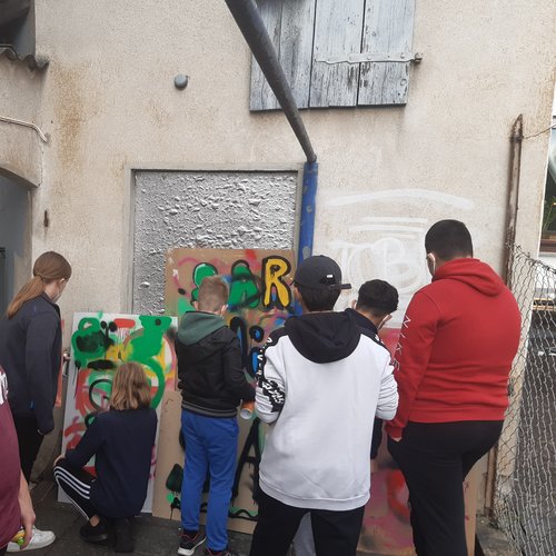 Kinder und Jugendliche besprühen beim Graffitti-Workshop Kartons vor einer Hauswand
